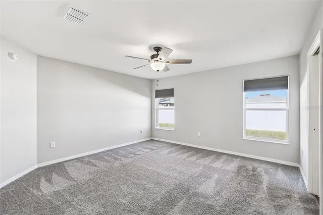 an empty room with a chandelier fan and windows