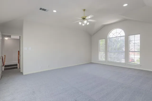 an empty room with chandelier fan and windows
