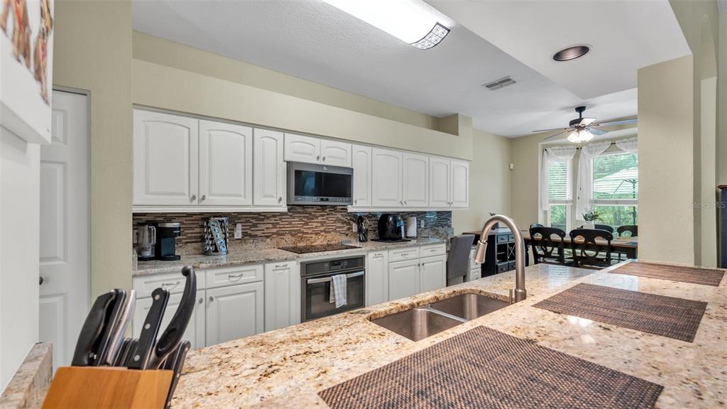 2803 Spring Meadow Drive Plant City, FL 33566 - Photo 20 of 74 a kitchen with stainless steel appliances granite countertop a stove top oven a sink a dining table and chairs with white cabinets