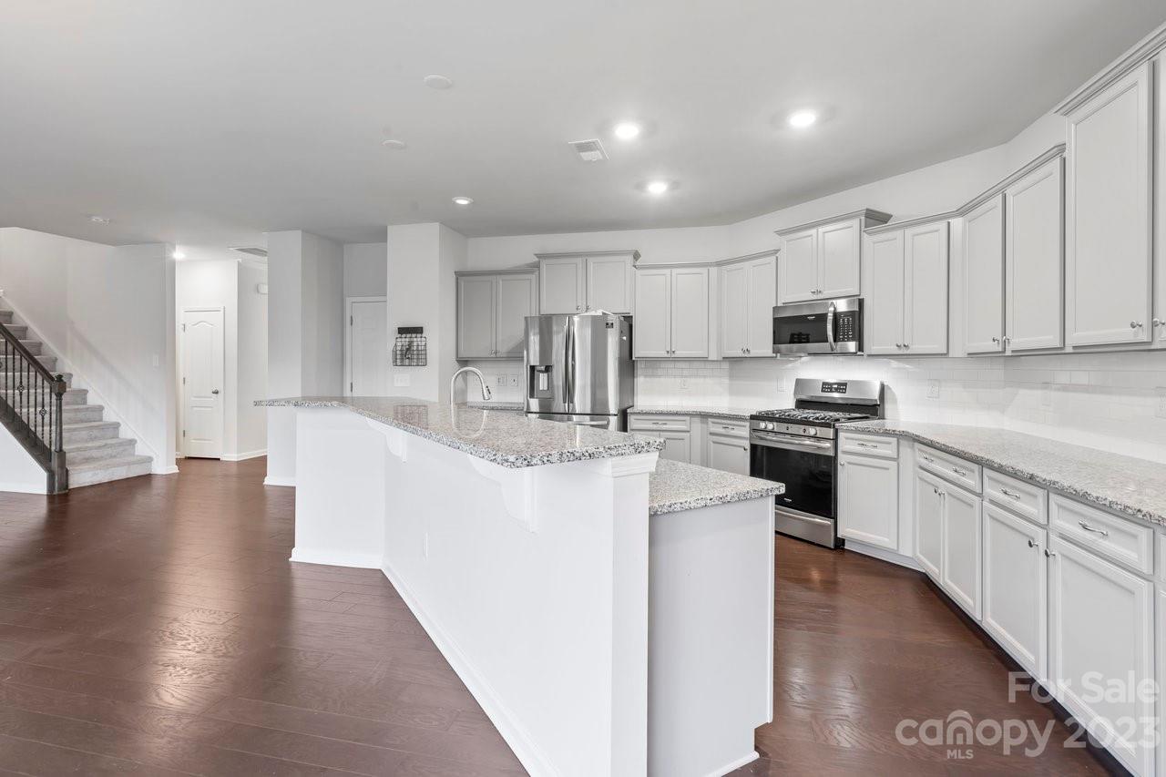 18209 Kalabash Road Charlotte, NC 28278 - Photo 11 of 48 a kitchen with stainless steel appliances granite countertop a stove top oven a sink a refrigerator white cabinets and couches with wooden floor
