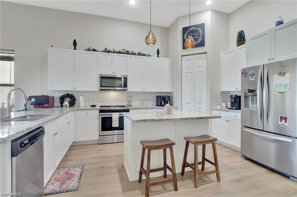 5123 Genoa Street Ave Maria, FL 34142 - Photo 6 of 34 a kitchen with stainless steel appliances granite countertop a stove top oven a sink a refrigerator and white cabinets with wooden floor
