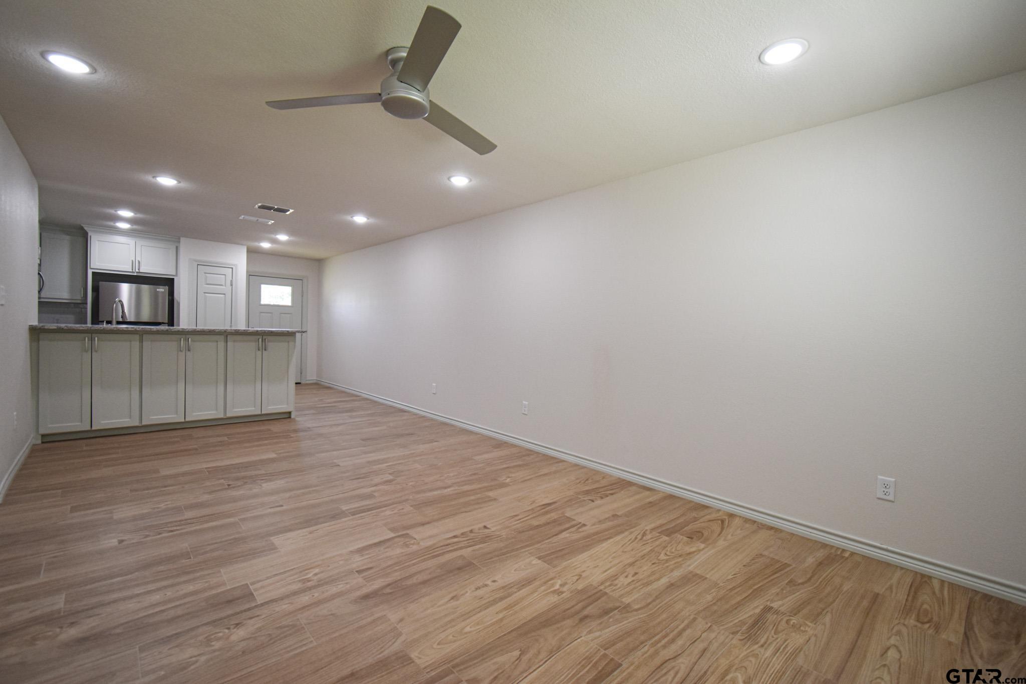 1417 East Earle Street Tyler, TX 75702 - Photo 5 of 31 an empty room with wooden floor and kitchen view