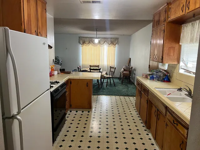 a kitchen with granite countertop a refrigerator a stove a sink dishwasher and a dining table with wooden floor