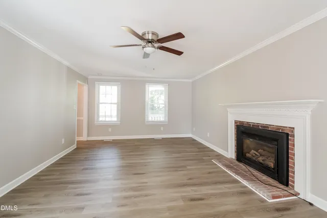 a view of an empty room with wooden floor fireplace and a window