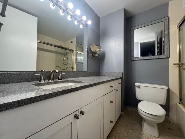 a bathroom with a granite countertop toilet sink and mirror
