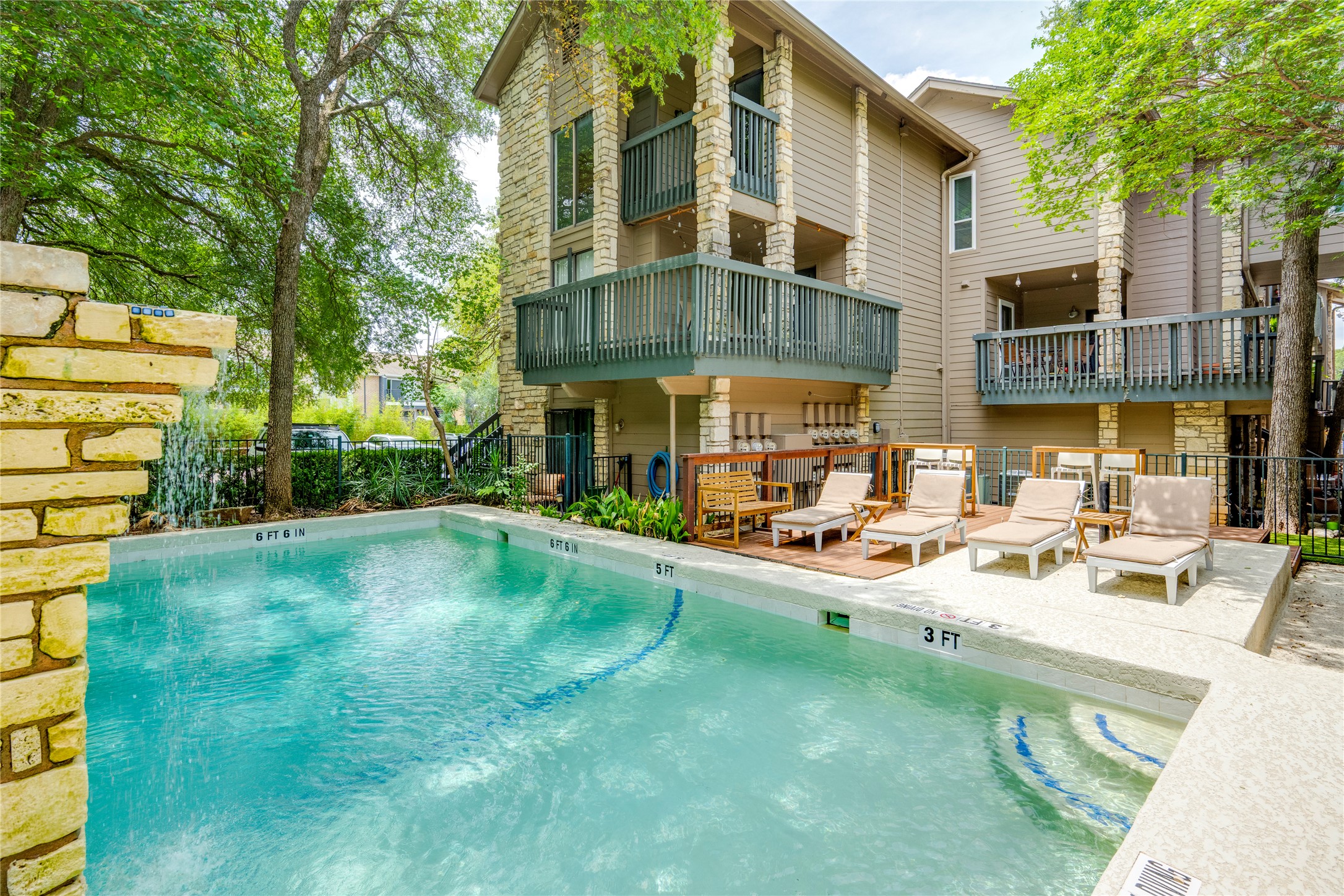 3627 Menchaca Road, Unit 214 Austin, TX 78704 - Photo 27 of 28 A tranquil community pool with ample lounge seating awaits beside a multi-story building featuring stone accents and private balconies.