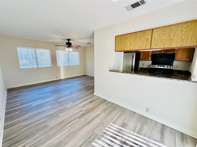 a view of an empty room with wooden floor and a ceiling fan