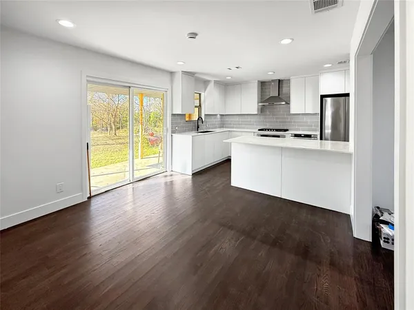 a kitchen with stainless steel appliances a stove top oven a sink and white cabinets with wooden floor