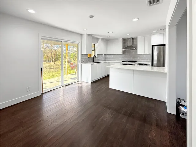 a kitchen with stainless steel appliances a stove top oven a sink and white cabinets with wooden floor