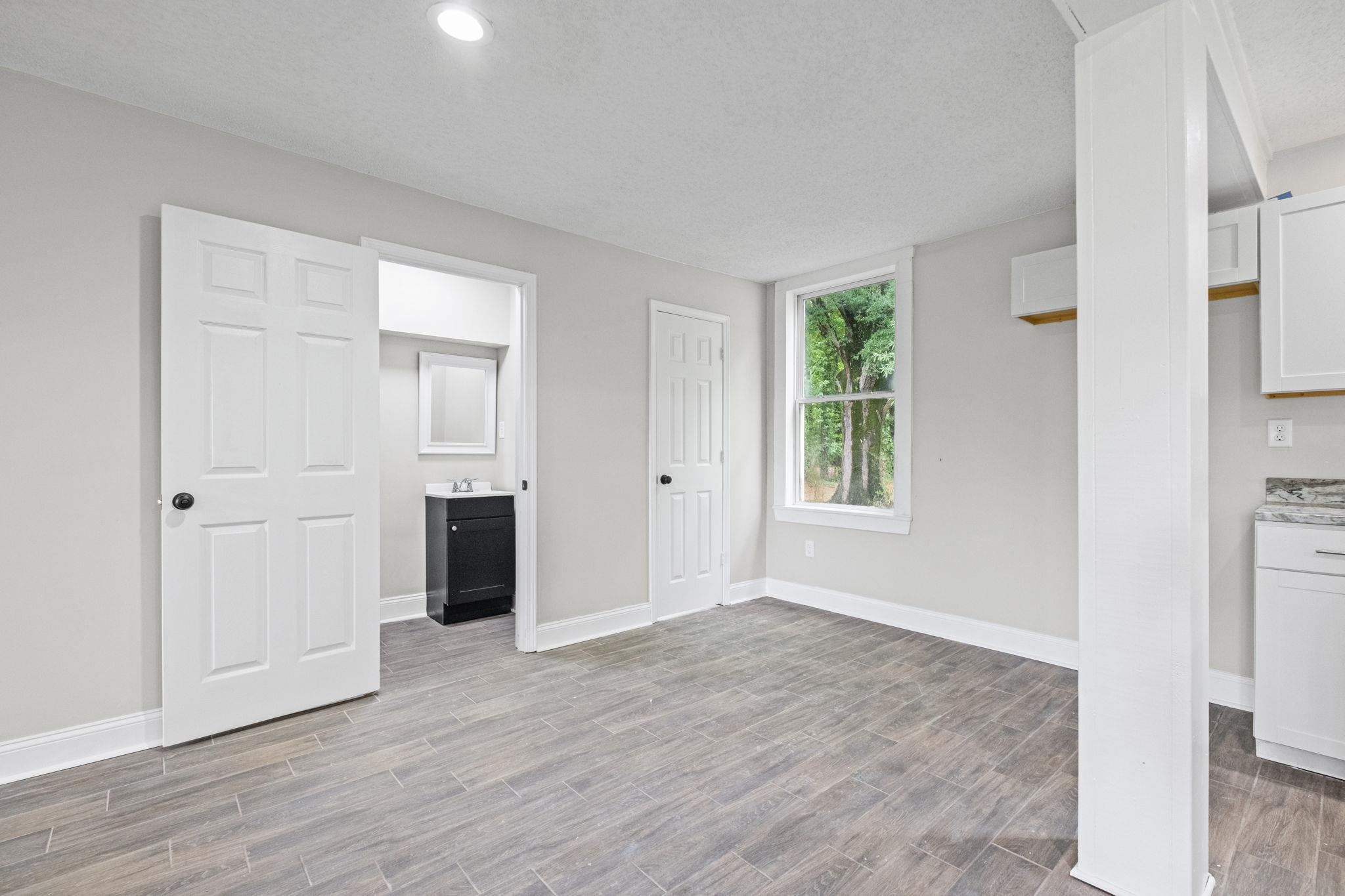 5843 Stewart Road Lakeland, TN 38002 - Photo 11 of 26 Interior space with wood-finish flooring, recessed lighting, and a white six-panel door leading to a bathroom featuring a dark wood vanity with a white countertop and mirror