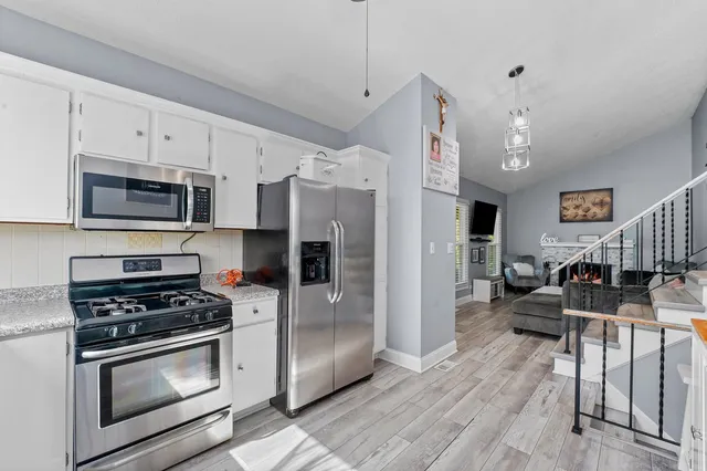 a kitchen with stainless steel appliances a stove a sink a refrigerator white cabinets a dining table and chairs