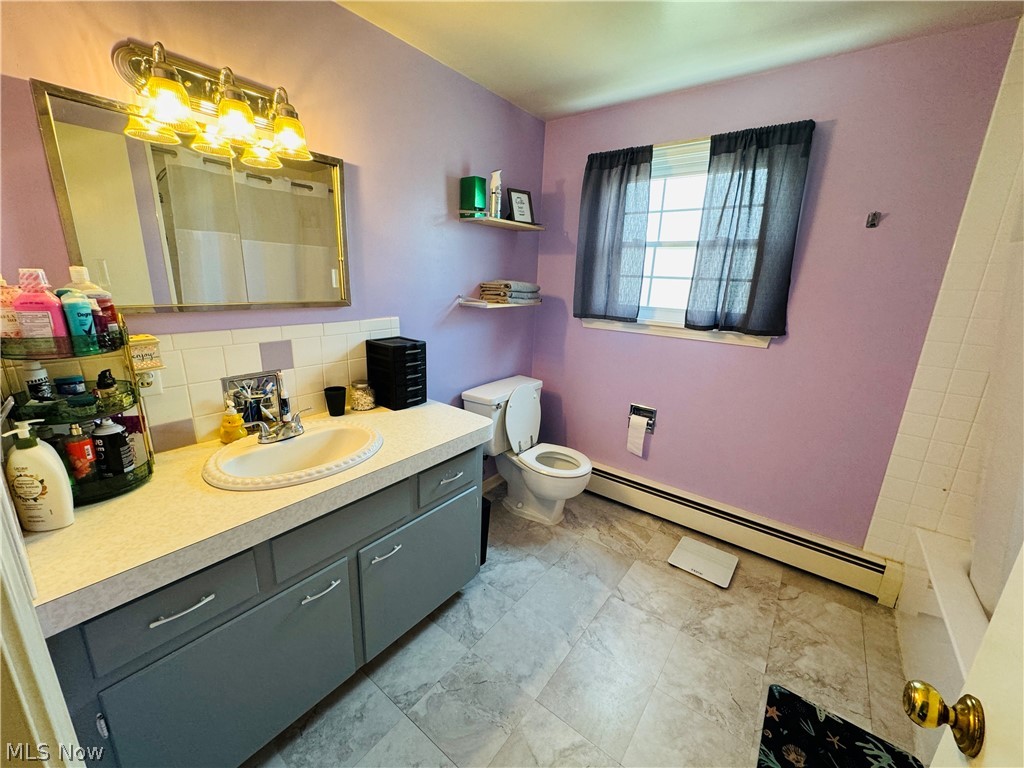 9531 West Ridge Road Elyria, OH 44035 - Photo 23 of 32 Bathroom with backsplash, tile floors, a baseboard radiator, toilet, and vanity