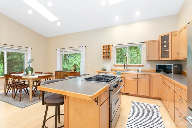 a kitchen with a stove a sink a counter top space and living room filled with windows