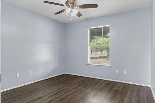 an empty room with wooden floor chandelier fan and windows