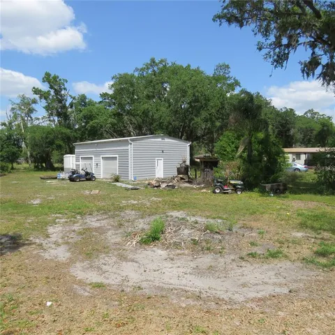 a white house with a big yard and large trees with wooden fence