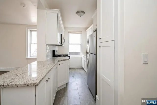 a kitchen with granite countertop a refrigerator a sink and white cabinets