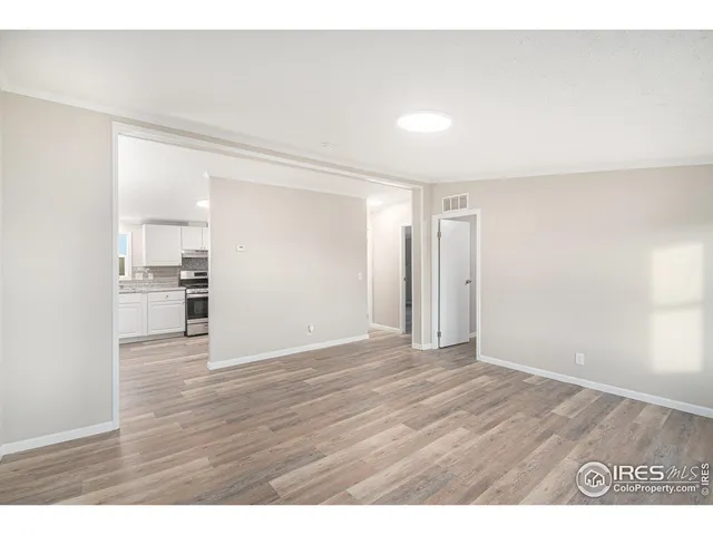 a view of an empty room and kitchen with wooden floor