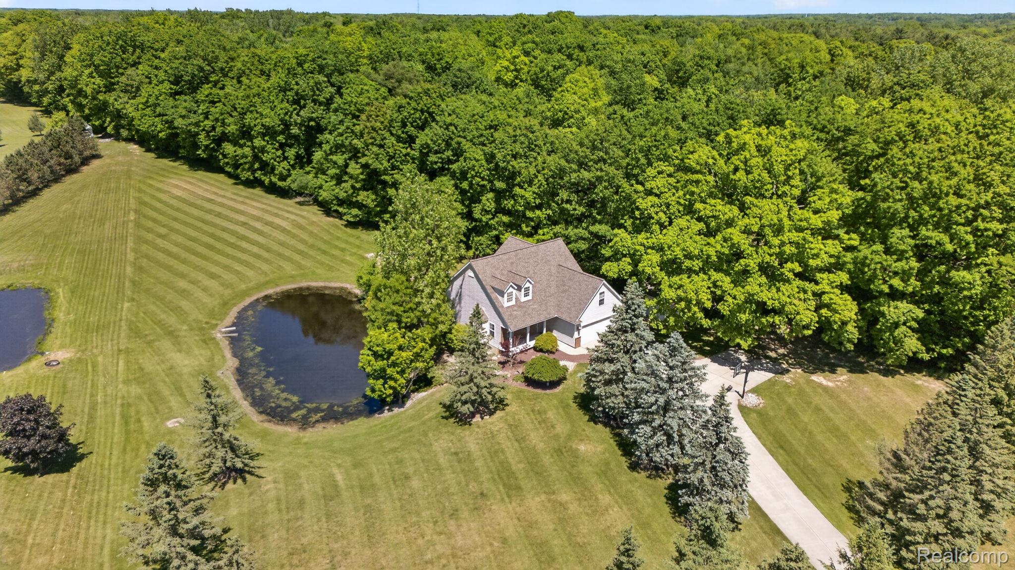 9055 Hegel Road Grand Blanc, MI 48439 - Photo 55 of 62 Spacious property featuring a light gray exterior residence with a brown shingle roof, two distinct ponds, a long paved driveway, and extensive surrounding woodlands