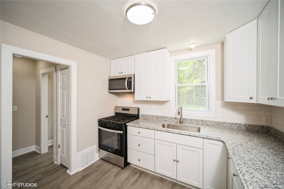 2188 North Taylor Road Cleveland Heights, OH 44112 - Photo 6 of 15 Kitchen featuring appliances with stainless steel finishes, wood finished floors, white cabinetry, and light stone counters