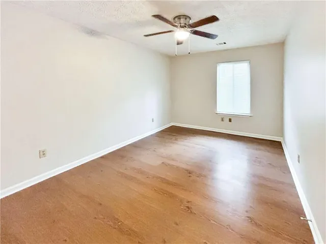 an empty room with wooden floor fan and windows