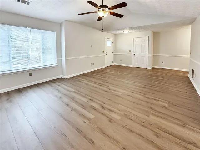 an empty room with wooden floor chandelier fan and windows