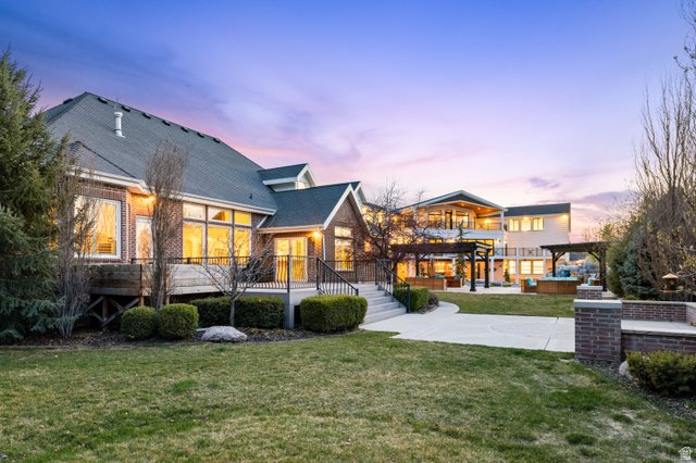 1263 Chapman Court Alpine, UT 84004 - Photo 13 of 83 Back of house at dusk featuring a yard, a shingled roof, a patio area, a balcony, and brick siding