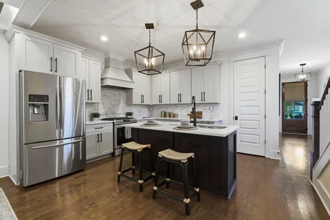 a kitchen with stainless steel appliances granite countertop a refrigerator a sink dishwasher a stove and white cabinets with wooden floor