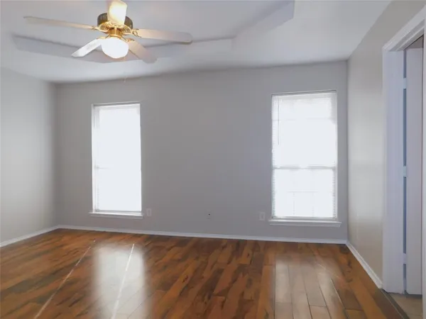 an empty room with wooden floor chandelier fan and windows