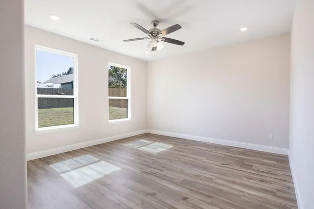 an empty room with wooden floor fan and windows
