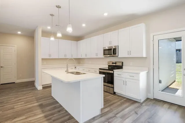 a kitchen with a sink stainless steel appliances and wooden floor