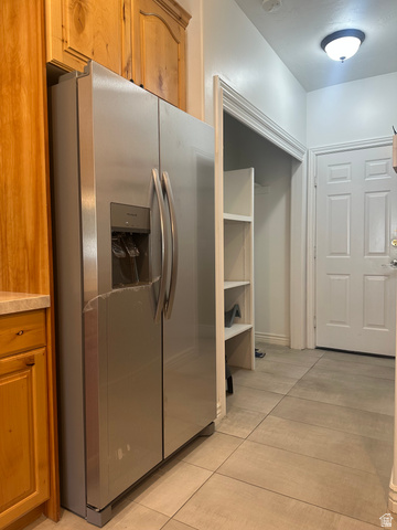 Stainless steel side-by-side refrigerator, wood cabinetry, light-toned tiled flooring, built-in shelving, and a paneled door