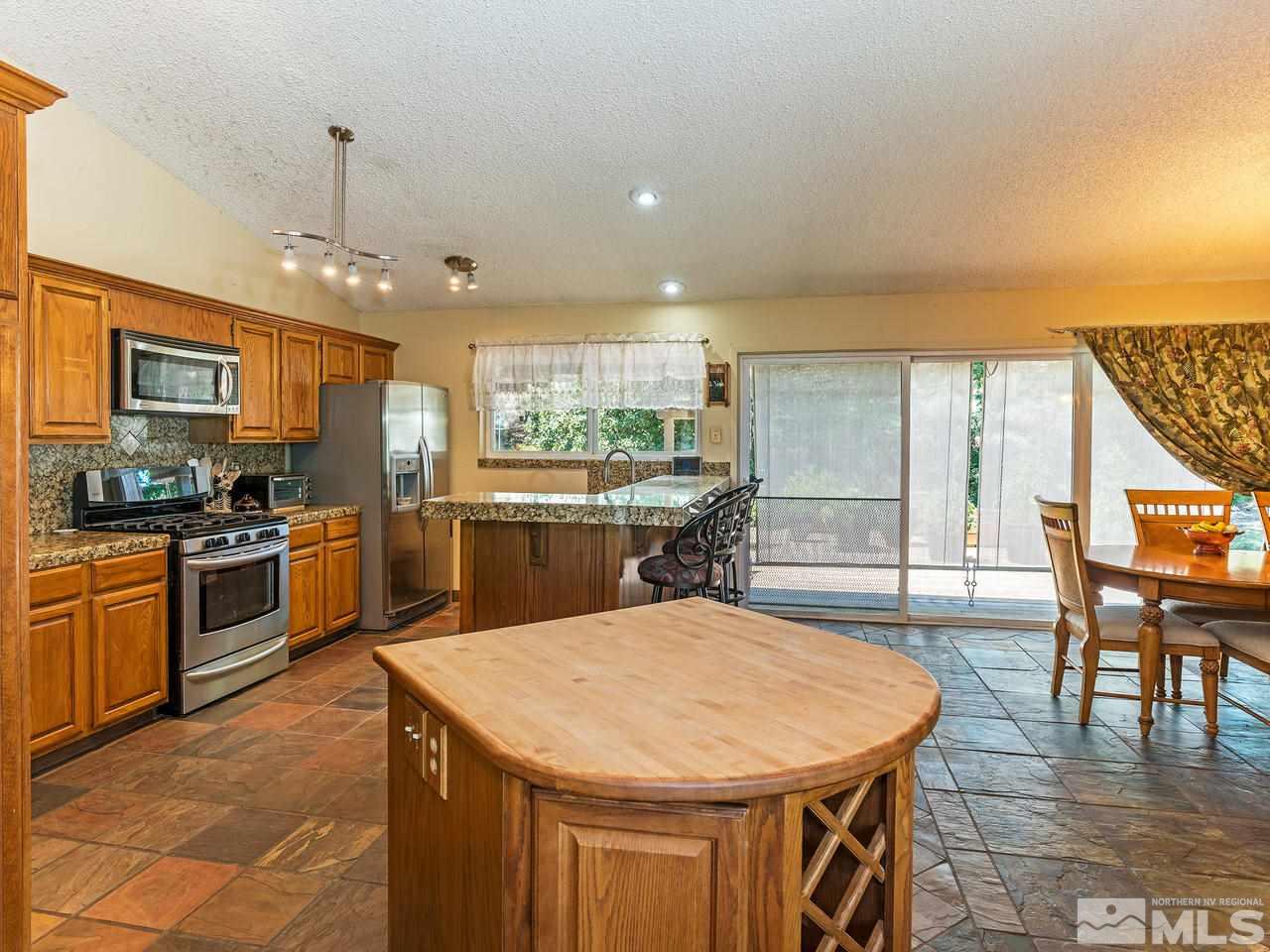 13055 Thomas Creek Road Reno, NV 89511 - Photo 7 of 24 a kitchen with stainless steel appliances kitchen island granite countertop a stove a sink a microwave a dining table and chairs with wooden floor