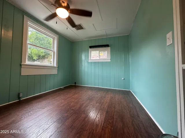 an empty room with wooden floor chandelier fan and windows