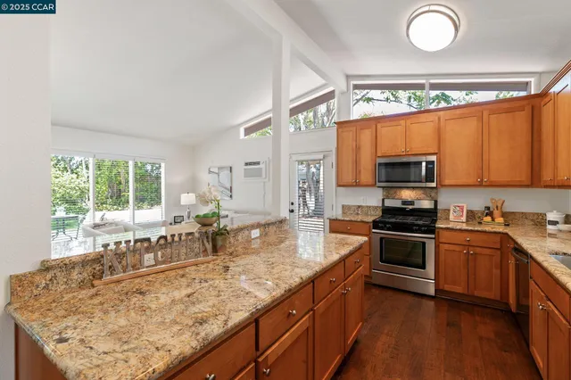 a kitchen with stainless steel appliances granite countertop wooden cabinets a stove top oven a sink and dishwasher with wooden floor