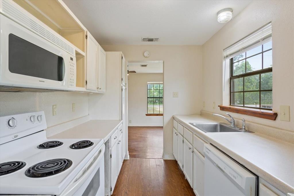 608 9th Street Hico, TX 76457 - Photo 10 of 23 Kitchen featuring white cabinetry, wood-finish flooring, white appliances including a range and over-range microwave, and a double basin sink