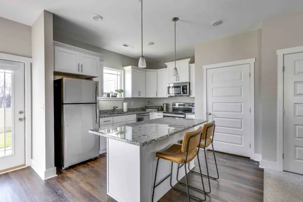 a kitchen with stainless steel appliances granite countertop a refrigerator a sink dishwasher a stove a refrigerator and white cabinets with wooden floor