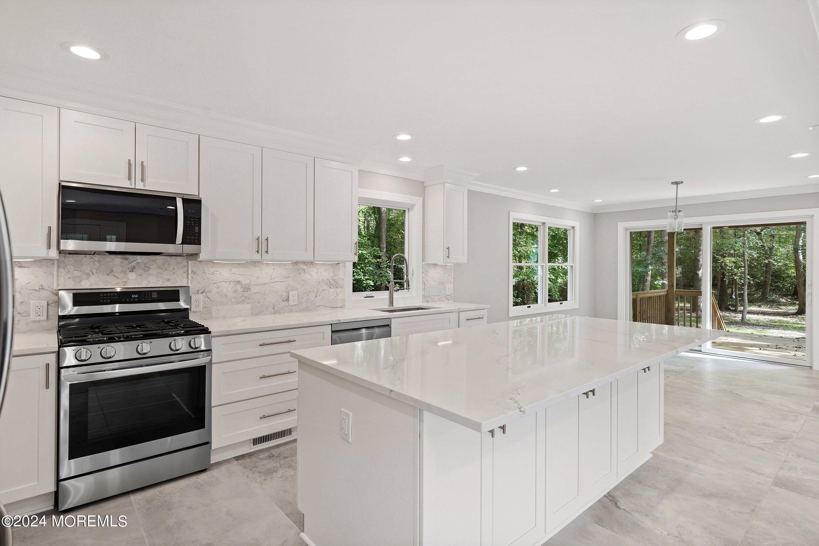 a large white kitchen with stainless steel appliances granite countertop a stove a sink and a microwave