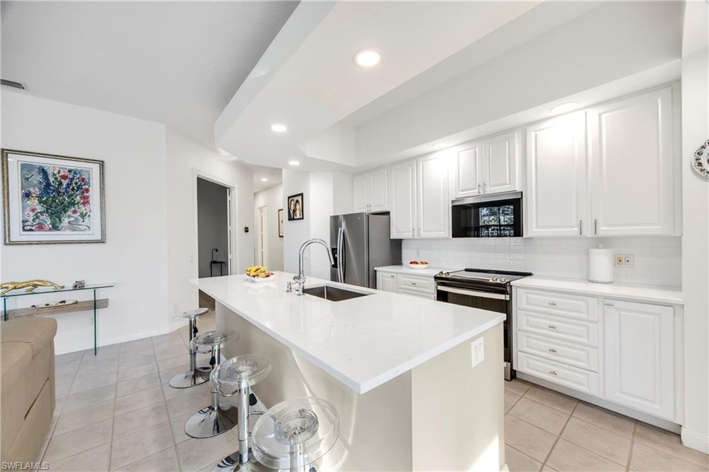 4708 Rio Poco Court Naples, FL 34109 - Photo 9 of 37 Kitchen with a kitchen bar, stainless steel appliances, white cabinets, light tile patterned floors, and light stone countertops