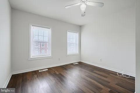 an empty room with wooden floor chandelier fan and windows