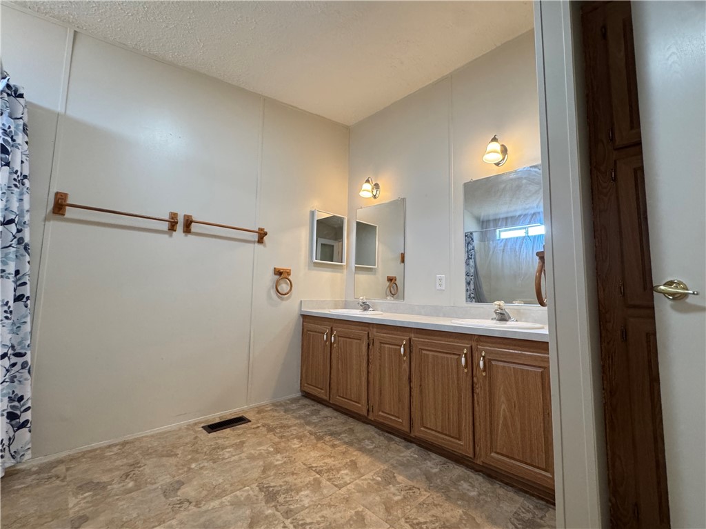 14224 East Randy Ranch Road Kingman, AZ 86401 - Photo 17 of 75 The bathroom features a double vanity with wood cabinetry, individual mirrors and sconce lighting, and a patterned shower curtain