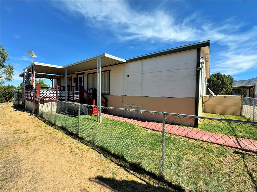 14224 East Randy Ranch Road Kingman, AZ 86401 - Photo 2 of 75 The property features a covered porch with a red railing and decorative white panels, a fenced yard with grass and a red paved path, and a light-colored exterior with a darker base