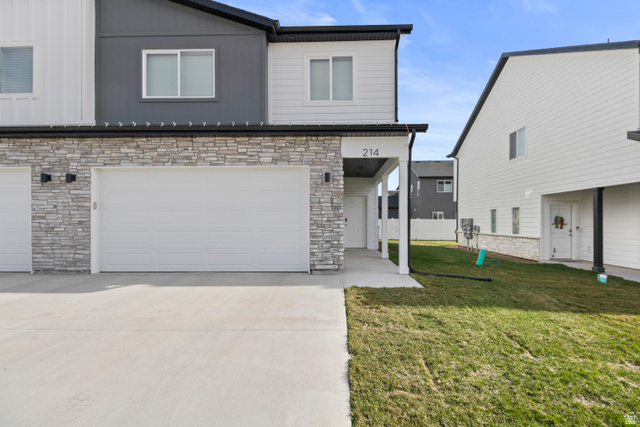 1262 West 500 South Logan, UT 84321 - Photo 36 of 39 Modern townhome exterior featuring a two-car garage, stone veneer siding, fiber cement paneling, and a covered entryway