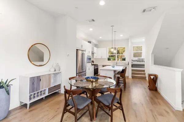 a kitchen with stainless steel appliances a stove a refrigerator a sink a dining table and chairs with wooden floor