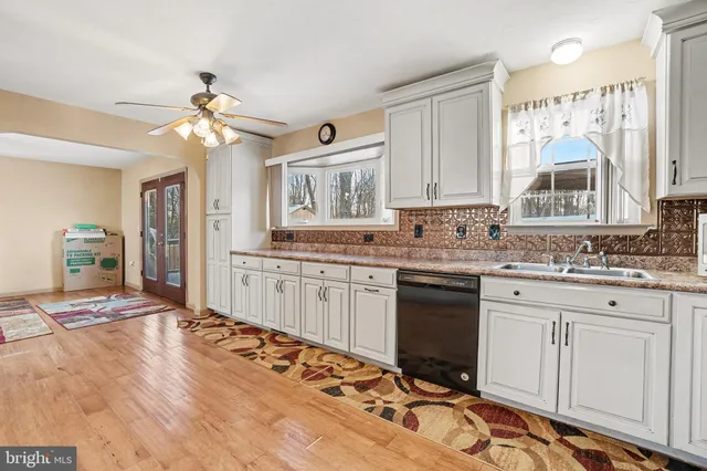 a kitchen with stainless steel appliances granite countertop a stove a sink dishwasher and white cabinets with wooden floor