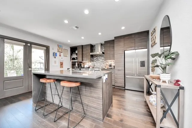 a kitchen with stainless steel appliances granite countertop a refrigerator a sink dishwasher a dining table and chairs with wooden floor