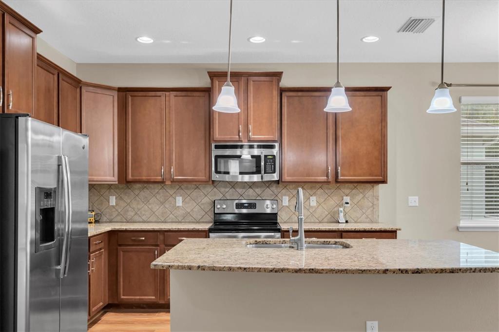 11236 Merganser Way New Port Richey, FL 34654 - Photo 5 of 41 a kitchen with stainless steel appliances granite countertop a refrigerator a sink a stove a microwave and wooden cabinets