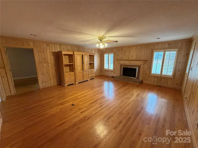 an empty room with wooden floor fireplace and windows
