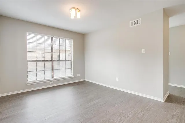 an empty room with wooden floor and windows with curtains