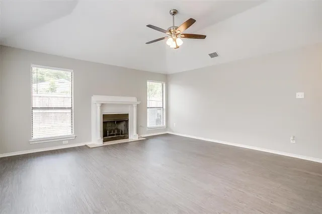 an empty room with chandelier fan and windows