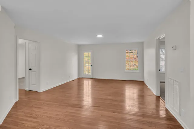 a view of an empty room with wooden floor and window